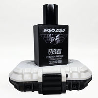 Bravo Zulu VIXEN Extrait de Parfum bottle by Flagship Soap Company balanced on top of its closed white rugged tactical case, the matte black glass bottle displaying the silver BRAVO ZULU B★Z winged logo and VIXEN name, on a seamless white studio background.