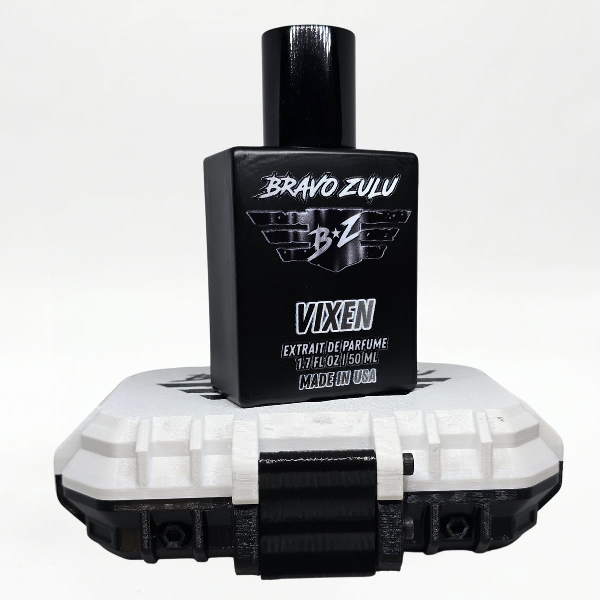 Bravo Zulu VIXEN Extrait de Parfum bottle by Flagship Soap Company balanced on top of its closed white rugged tactical case, the matte black glass bottle displaying the silver BRAVO ZULU B★Z winged logo and VIXEN name, on a seamless white studio background.