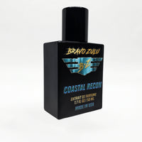 Angled three-quarter studio shot of the Bravo Zulu COASTAL RECON Extrait de Parfum bottle by Flagship Soap Company, showing the matte black glass bottle and black cap with turquoise-and-gold BRAVO ZULU B★Z winged logo and COASTAL RECON branding, set against a seamless white studio background.