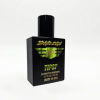 Bravo Zulu TIPSY Extrait de Parfum bottle by Flagship Soap Company balanced on top of its closed black rugged tactical case, the matte black glass bottle displaying the lime-green BRAVO ZULU B★Z winged logo and TIPSY name, on a seamless white studio background.
