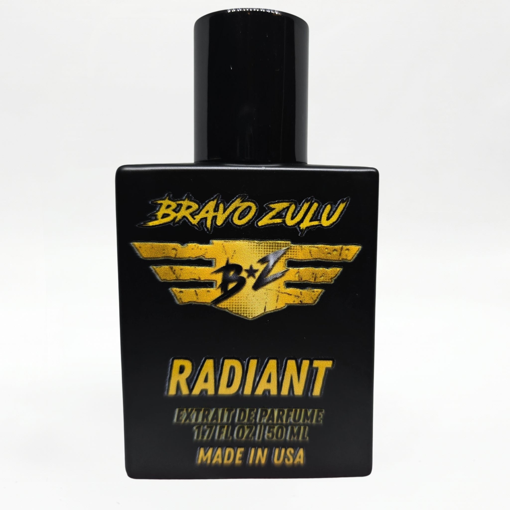 Front-facing studio product shot of Bravo Zulu RADIANT Extrait de Parfum by Flagship Soap Company. The heavy matte black glass bottle with matching black cap is centered on a clean white background, displaying the gold-and-black BRAVO ZULU B★Z winged logo, RADIANT name, Extrait de Parfume 1.7 FL OZ / 50 ML, and Made in USA text.