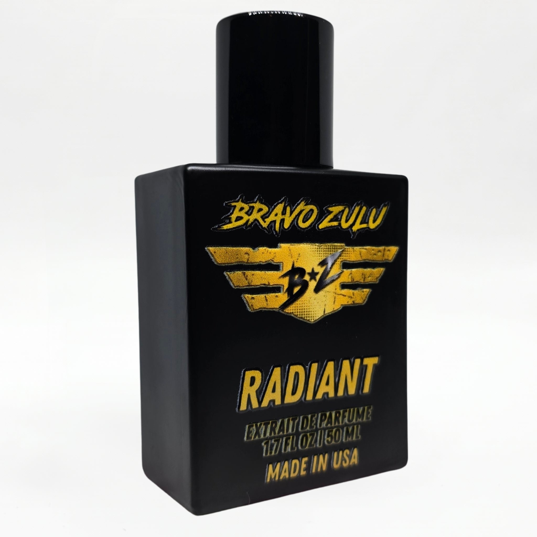 Angled studio shot of the Bravo Zulu RADIANT Extrait de Parfum bottle by Flagship Soap Company, showing the matte black glass bottle and black cap with gold-and-black BRAVO ZULU B★Z winged logo and RADIANT branding, set against a seamless white studio background.