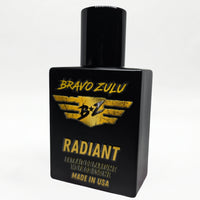 Bravo Zulu RADIANT Extrait de Parfum bottle by Flagship Soap Company balanced on top of its closed yellow-and-black rugged tactical case, the matte black glass bottle displaying the gold BRAVO ZULU B★Z winged logo and RADIANT name, on a seamless white studio background.