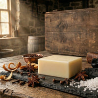 Close-up of 1776 Natural Cold Processed Men's Soap bar with raw ingredients including star anise, whole cloves, activated charcoal, and sea salt on a rustic colonial workbench.