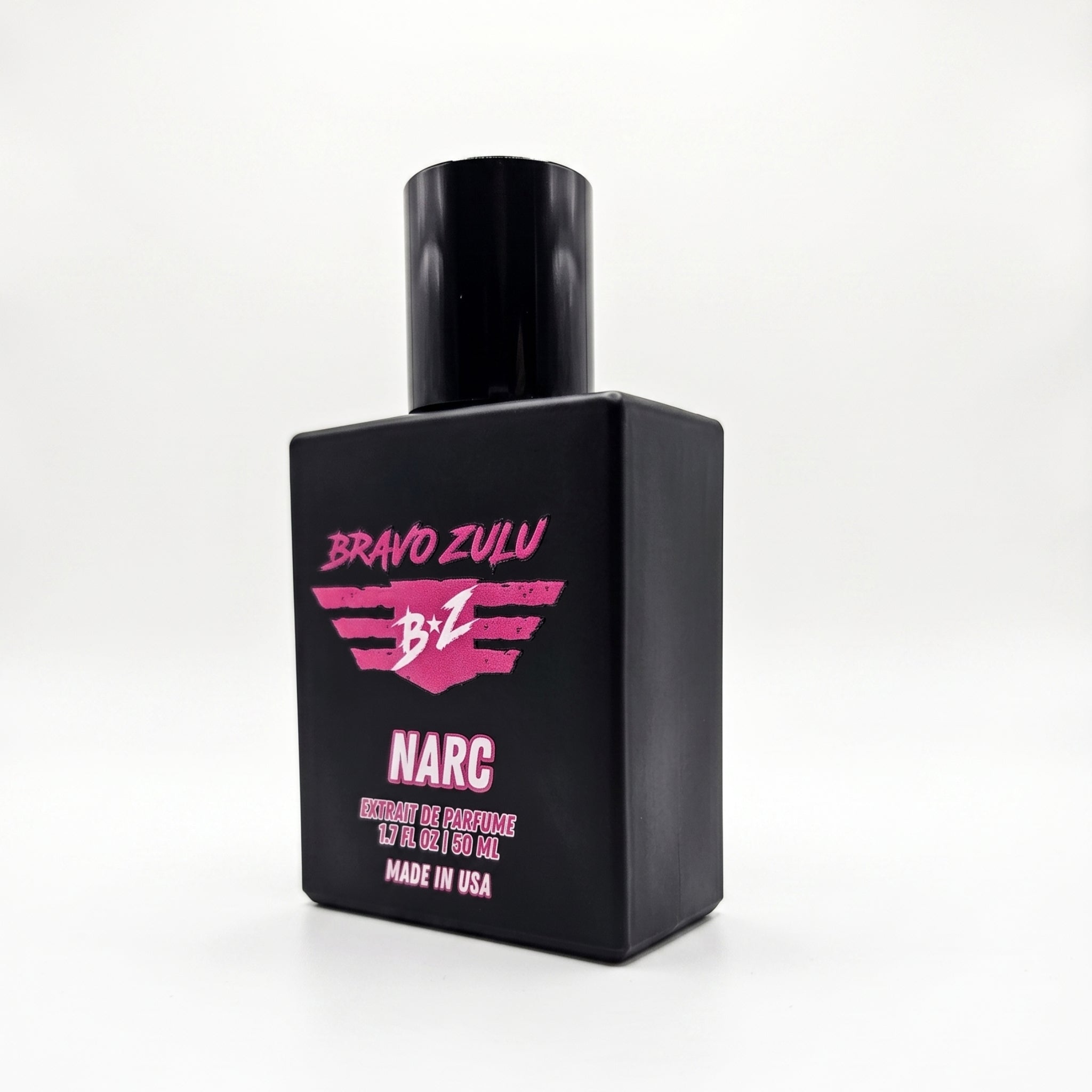 An angled product shot of the Bravo Zulu NARC Extrait de Parfum men's cologne bottle isolated on a seamless white background. The heavy tactical matte black glass bottle is shown from a three-quarter perspective, cleanly displaying the rugged pink and white "B-Z NARC" branding and "Made in USA" label text.