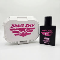 Front studio product shot of the Bravo Zulu NARC Extrait de Parfum men's cologne bottle standing next to its closed custom protective tactical case, isolated on a seamless white background. The heavy matte black glass fragrance bottle and the rugged white case both cleanly display the bold pink "B★Z" stenciled wing logo, capturing a premium, high-stakes undercover edge.