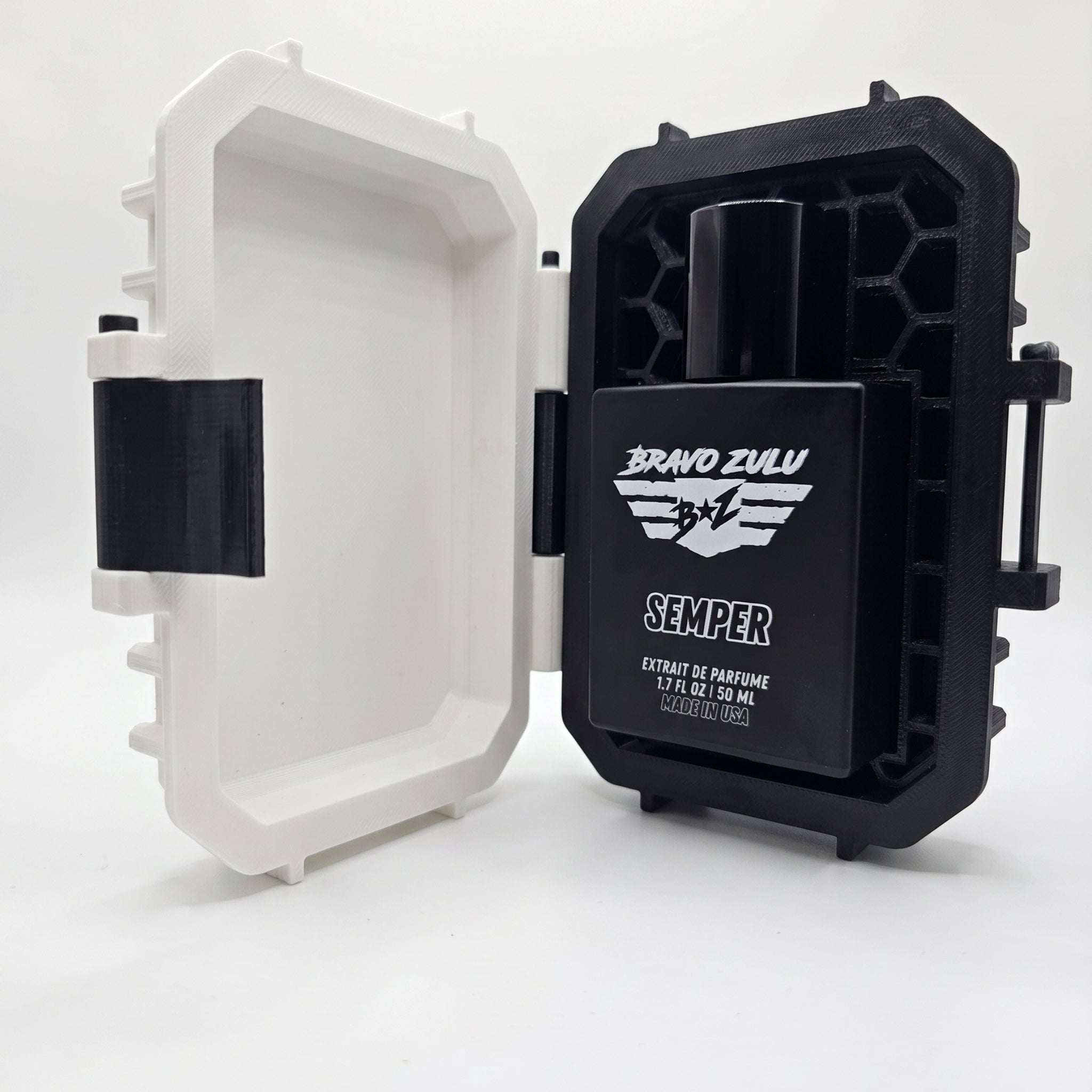 An open, custom-engineered rugged protective case showcasing the SEMPER Extrait de Parfum bottle by Bravo Zulu on a clean white background. The heavy matte black glass bottle is securely locked inside the black textured, hexagonal-patterned interior of the tactical case, which features a stark Vanguard White exterior lid. This premium 30% concentration, American-built cologne delivers a dominant, unyielding scent profile of cold ocean marine, rugged earthy woods, and sharp citrus.