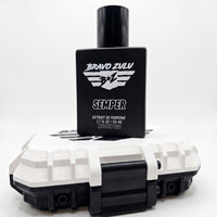 A high-contrast e-commerce product shot of SEMPER Extrait de Parfum by Bravo Zulu on a seamless white studio background. The heavy matte black glass bottle is stacked directly on top of its custom-engineered, rugged tactical case, which features a stark Vanguard White lid and aggressive matte black latches. The bottle cleanly displays the white flight-wing logo and bold branding for this premium, American-built men's cologne, engineered for a commanding and unyielding presence.
