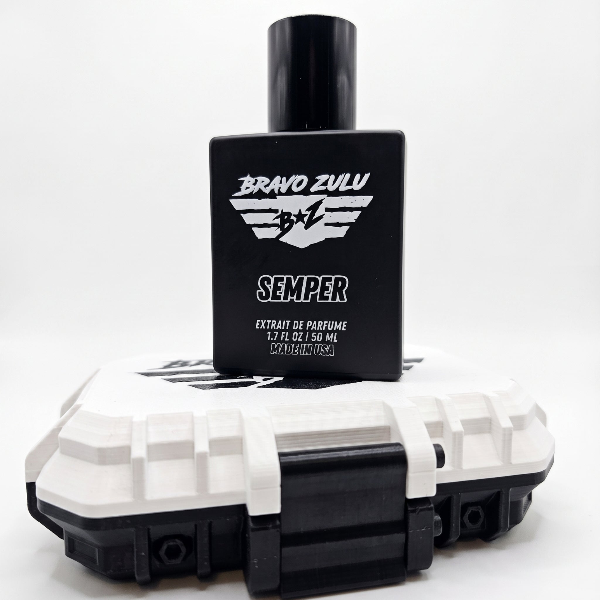 A high-contrast e-commerce product shot of SEMPER Extrait de Parfum by Bravo Zulu on a seamless white studio background. The heavy matte black glass bottle is stacked directly on top of its custom-engineered, rugged tactical case, which features a stark Vanguard White lid and aggressive matte black latches. The bottle cleanly displays the white flight-wing logo and bold branding for this premium, American-built men's cologne, engineered for a commanding and unyielding presence.