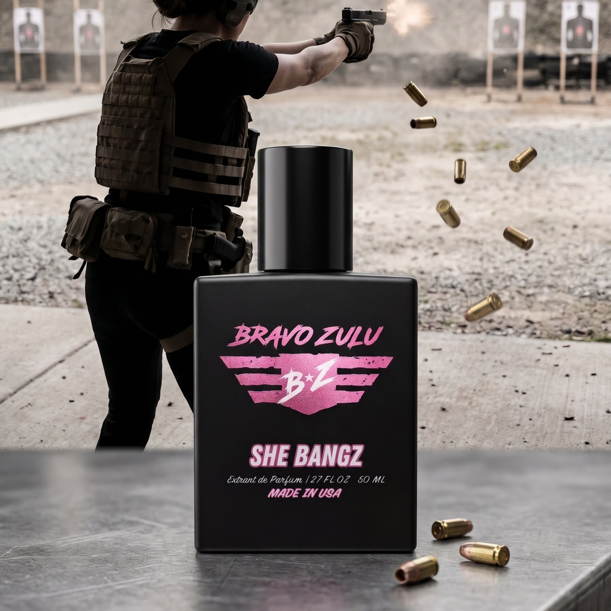 Bravo Zulu Flagship Soap Company SHE BANGZ Extrait De Parfum (Bravo Zulu Lineup) for women, a powerful, commanding, high-yield gourmand fragrance. The heavy, matte black glass bottle, designed with a premium American-built, mission-first mindset, is centered. The label features pink branding and lists 'Extrait de Parfum / 2.7 FL OZ 50 ML' and 'MADE IN USA'. A woman in tactical gear is firing a pistol at the shooting range in the background, with shell casings ejecting and two rounds on the table next to the