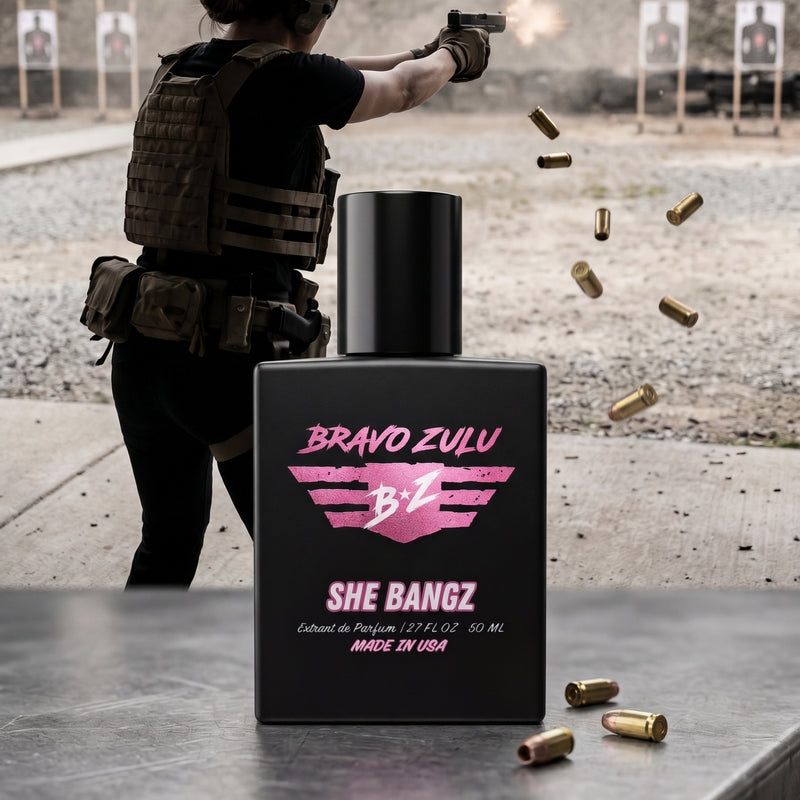 Bravo Zulu Flagship Soap Company SHE BANGZ Extrait De Parfum (Bravo Zulu Lineup) for women, a powerful, commanding, high-yield gourmand fragrance. The heavy, matte black glass bottle, designed with a premium American-built, mission-first mindset, is centered. The label features pink branding and lists 'Extrait de Parfum / 2.7 FL OZ 50 ML' and 'MADE IN USA'. A woman in tactical gear is firing a pistol at the shooting range in the background, with shell casings ejecting and two rounds on the table next to the