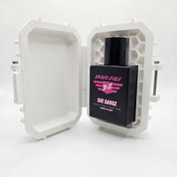 product image of SHE BANGZ Extrait de Parfum from the Bravo Zulu Lineup by Flagship Soap Company. The heavy, tactical matte black glass bottle is showcased sitting securely upright inside its open, custom-engineered rugged protective tactical case. The clean white case features a distinct internal honeycomb security architecture. Isolated on a seamless, brilliant white background, the sleek black bottle displays vibrant hot pink branding for "BRAVO ZULU" and "SHE BANGZ." The label marks its high-impact 30% 