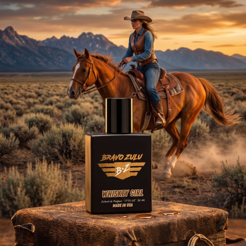 A prominent, front-facing product shot of the Bravo Zulu Whiskey Girl Extrait de Parfum bottle sits anchored on a distressed leather surface, featuring warm amber liquid drops. In the background, a woman in Western attire—cowboy hat, leather vest, and denim—rides a light-brown horse across a sagebrush desert valley during a vibrant sunset over mountains. The scene captures the scent’s untamed depth, inspired by the rugged independence of the American heartland.