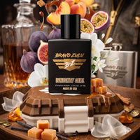 Flagship Soap Company's Whiskey Girl perfume bottle displayed with its key scent architecture ingredients. Visual elements of warm caramelized sugar, rich maple syrup, fresh peach, passionfruit, dark Mediterranean fig, jasmine, and vanilla pod explode around the tactical matte black bottle and rugged Bourbon Brown custom case, illustrating the complex wood-and-fruit profile of this 30% concentration Extrait de Parfum.
