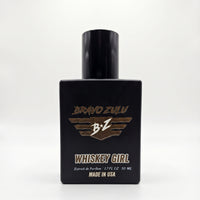 Front-facing view of Whiskey Girl Extrait de Parfum by Flagship Soap Company. The perfume is housed in a heavy, tactical matte black glass bottle featuring the gold-embossed Bravo Zulu wing logo. Below the logo, text reads "WHISKEY GIRL", "Extrait de Parfum | 1.7 FL OZ 50 ML", and "MADE IN USA", set against a clean, white background.