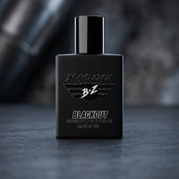 A professional product shot features the "BRAVO ZULU BLACKOUT" cologne, an aggressive, tactical masterpiece engineered for the men who defend the perimeter and hunt. Housed in a heavy, tactical matte black glass bottle built to block UV light, it presents an elite, monochromatic aesthetic designed to silenty take over. The bottle stands against a dark, moody background of rugged woods and deep shadows, reflecting the pitch-black musk, raw exotic woods, and gritty winter spices that form its unyielding, dang