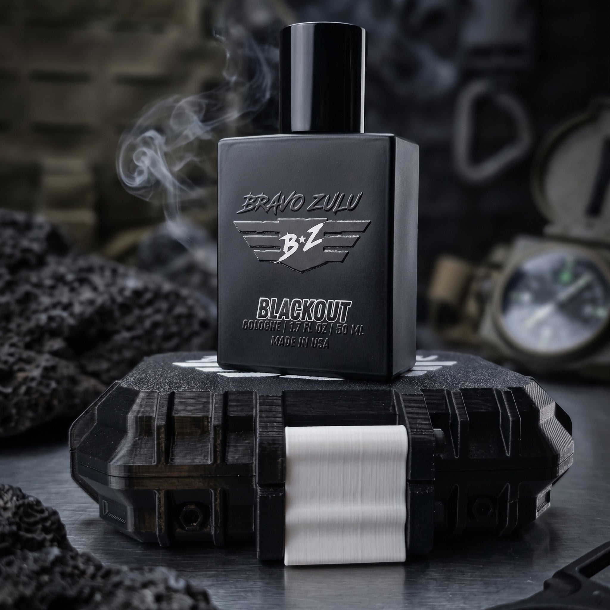 A gritty, atmospheric product shot featuring the BRAVO ZULU BLACKOUT cologne bottle standing upright on its closed tactical case against a dark, rugged background. Wisps of white smoke curl upward past the heavy matte black glass bottle, visually capturing the fragrance's intoxicating smoke screen profile of pitch-black musk, rugged woods, and heavy spices. The bottle prominently displays the embossed 'BRAVO ZULU' text and winged 'B+Z' logo, alongside silver text for 'BLACKOUT COLOGNE', '1.7 FL OZ / 50 ML',