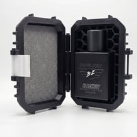 A bright, clean studio product shot on a white background highlighting the elite unboxing experience of the BLACKOUT Extrait de Parfum by Flagship Soap Company. The custom-engineered tactical case is propped completely open, showcasing its rugged monochromatic stealth black structure. The left lid is lined with protective gray foam and features a contrast white latch piece on the outer rim. On the right side, a specialized tactical honeycomb matrix shell perfectly encapsulates the heavy matte black glass co
