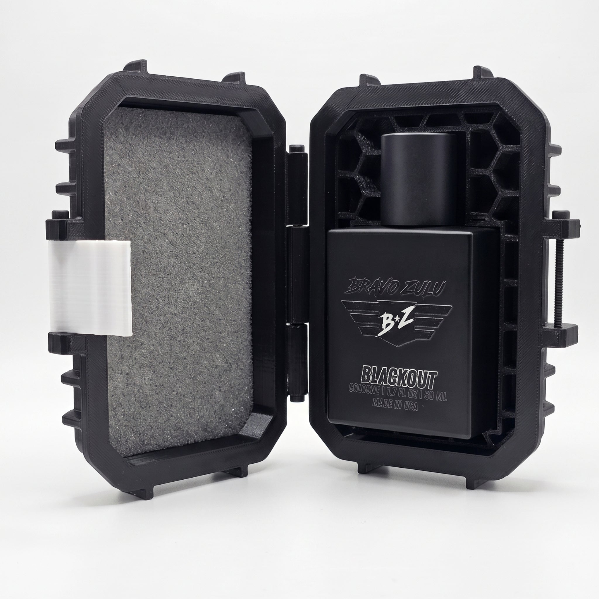 A bright, clean studio product shot on a white background highlighting the elite unboxing experience of the BLACKOUT Extrait de Parfum by Flagship Soap Company. The custom-engineered tactical case is propped completely open, showcasing its rugged monochromatic stealth black structure. The left lid is lined with protective gray foam and features a contrast white latch piece on the outer rim. On the right side, a specialized tactical honeycomb matrix shell perfectly encapsulates the heavy matte black glass co