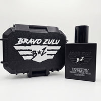 A clean e-commerce studio product shot on a crisp white background showing a side-by-side view of the premium hardware included with BLACKOUT Extrait de Parfum by Flagship Soap Company. On the left sits the closed, rugged custom-engineered stealth black tactical case featuring a prominent white embossed 'BRAVO ZULU' title and signature 'B+Z' winged logo design. Standing to the right is the heavy, tactical matte black glass bottle featuring an all-black cap. The front of the bottle displays the matching glos