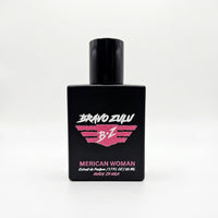 A straight, front-facing product shot of the Bravo Zulu MERICAN WOMAN Extrait de Parfum perfume bottle centered on a completely seamless, clean white background. The heavy, tactical matte black glass bottle is labeled with a bold pink and white winged B★Z logo and pink typography displaying the name and technical specifications. Formulated at a high-octane 30% fragrance oil concentration and proudly made in the USA, this premium blend features scent notes of sweet confectionary fruits, exotic midnight flora