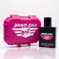 A side-by-side product display of the Bravo Zulu MERICAN WOMAN Extrait de Parfum perfume bottle standing next to its rugged custom protective case on a seamless, clean white reflective surface. The heavy tactical matte black glass bottle is positioned on the right, featuring a vibrant pink and white winged B★Z logo and pink branding text. To the left sits the closed custom-engineered tactical case finished in a striking Elite Pink with clean white contrast accents. Formulated at a high-octane 30% fragrance 