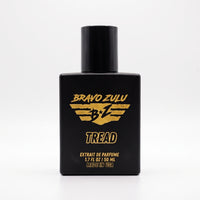 Tactical matte black glass bottle of TREAD Extrait de Parfum by Flagship Soap Company. Features a black atomizer cap and bold yellow Bravo Zulu branding, standing upright against a seamless white background.