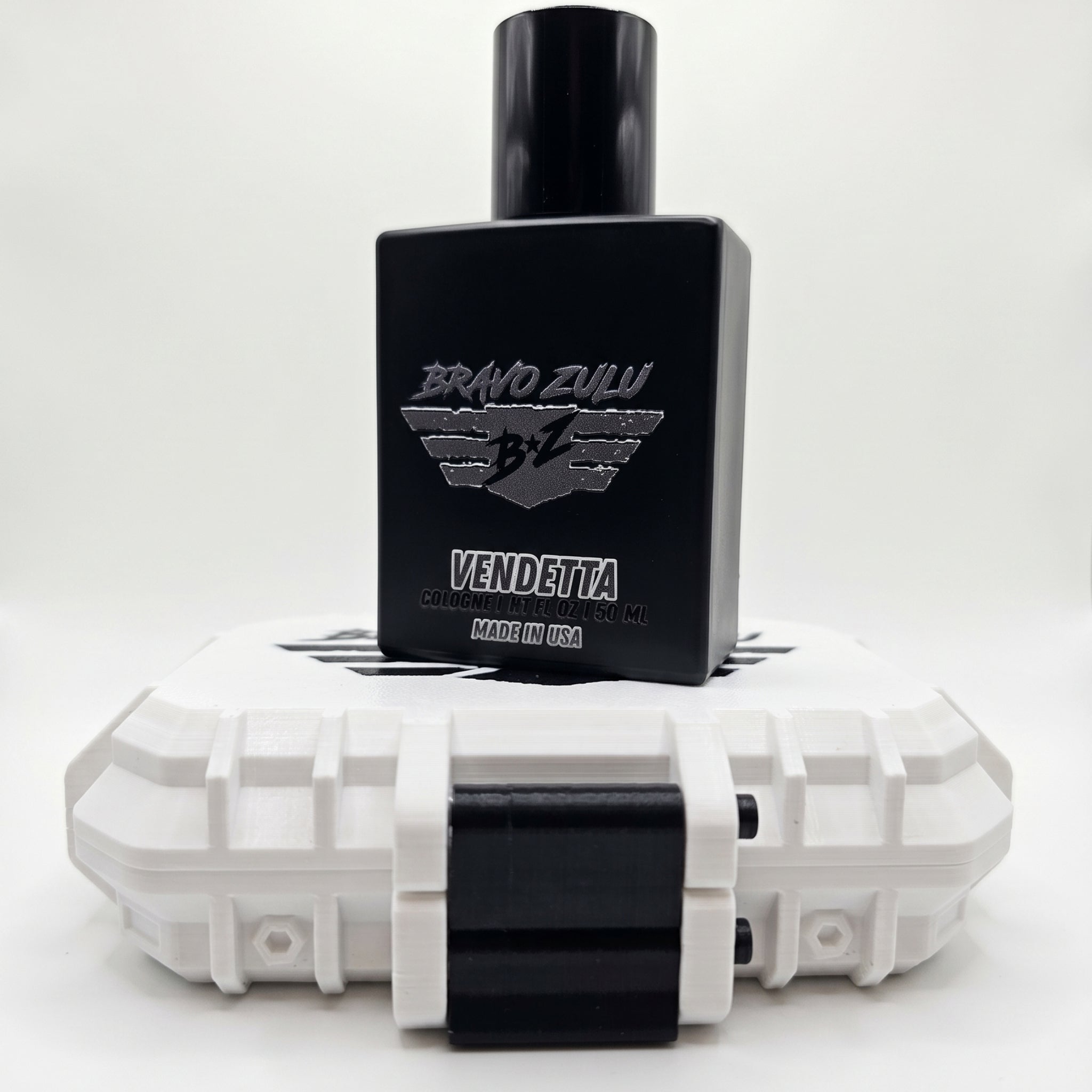 A tactical product display featuring the matte black glass bottle of Bravo Zulu VENDETTA Extrait de Parfum standing centered on top of its rugged, custom-engineered tactical case. The black bottle features a silver-embossed B★Z winged shield crest and the text "VENDETTA | COLOGNE | 1.7 FL OZ / 50 ML | MADE IN USA." The tactical fusion inside, a high-yield formula engineered for American grit and calculated precision, creates a wood-and-spice smoke screen locking onto the skin with 30% oil concentration. It 