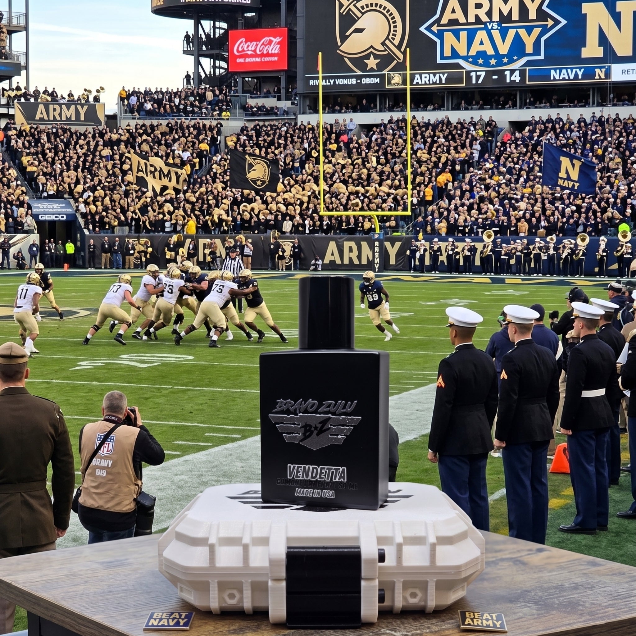 Alt Text: A high-impact product display featuring the Bravo Zulu VENDETTA cologne bottle and its custom rugged protective case centered in the foreground, set against the backdrop of the iconic Army-Navy football game stadium rivalry.

The heavy, tactical matte black glass bottle stands upright on top of its white protective case, which is positioned on a wooden table. The silver-embossed label on the front of the hardware displays the "BRAVO ZULU B★Z" winged shield insignia and the bold title text "VENDETT