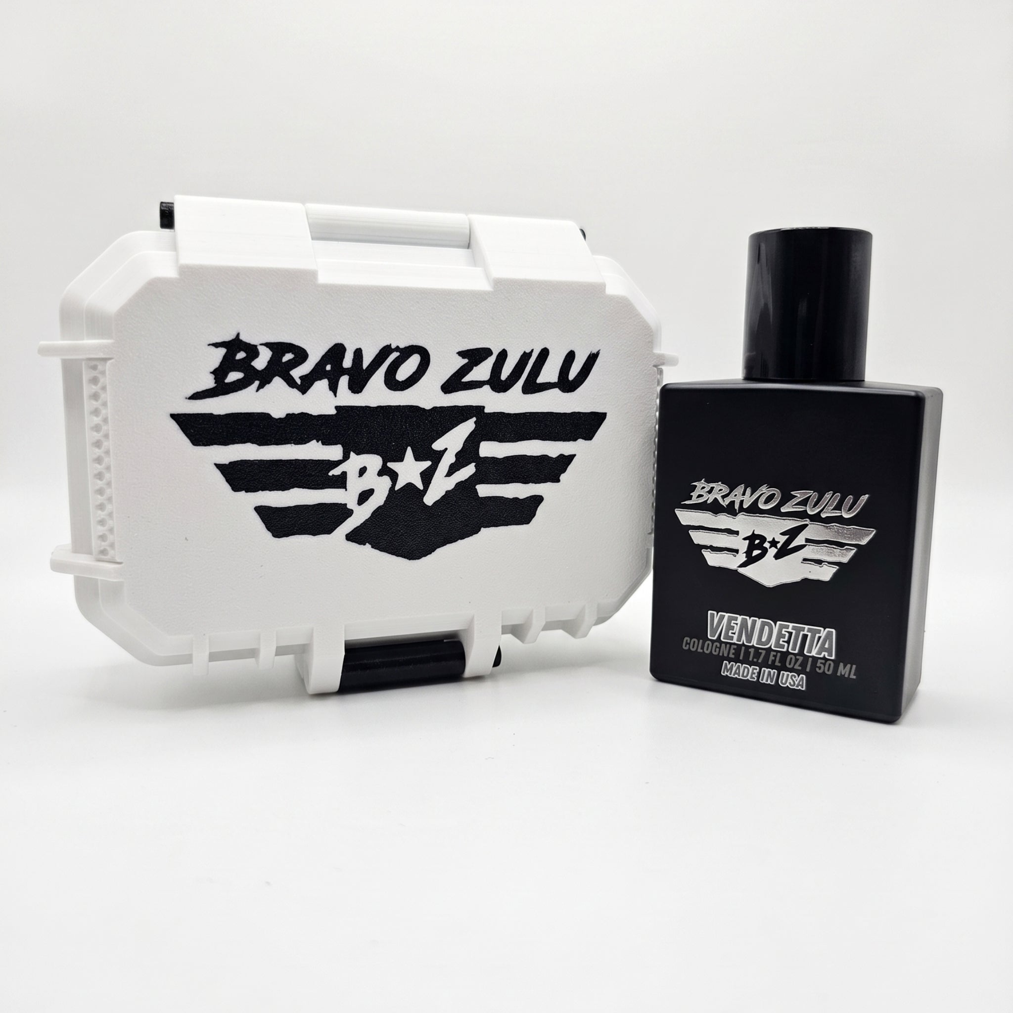 A professional product photograph showcasing the Bravo Zulu VENDETTA fragrance and its gift-ready custom case arranged side-by-side on a clean white background.

On the right stands the heavy, tactical matte black glass bottle designed to block out UV light and protect the integrity of the premium 30% Extrait de Parfum oils inside. The front of the bottle features silver-embossed branding with the "BRAVO ZULU B★Z" winged shield insignia and the bold title text "VENDETTA," detailed with "COLOGNE | 1.7 FL OZ 