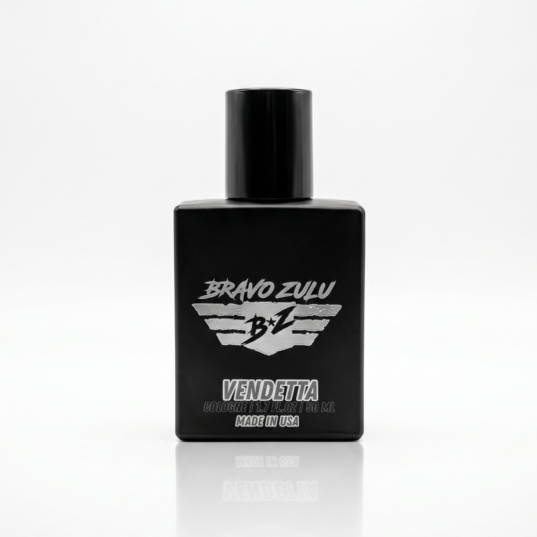 A high-resolution product photograph on a white background with a sharp reflection, featuring the Bravo Zulu VENDETTA Extrait de Parfum (cologne) bottle. The bottle is a matte black glass container with a glossy black cylindrical cap, designed with American grit and resilience for the man who handles business with calculated precision. The silver label on the front features the text "BRAVO ZULU" at the top, a stylized winged shield emblem with "B Z" on it, and "VENDETTA" in larger text below the emblem. At 