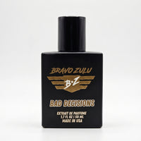 Bravo Zulu BAD DECISIONS Extrait de Parfum by Flagship Soap Company. A premium 30% concentration whiskey-themed men's cologne housed in a heavy tactical matte black glass bottle, centered against a clean, solid white studio background. The front display showcases the gold-textured Bravo Zulu logo and white "BAD DECISIONS" text, emphasizing an American-built, high-end masculine fragrance profile.