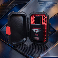 Bravo Zulu's 1776 Extrait de Parfum matte black cologne bottle showcased inside an open, rugged black and crimson red honeycomb tactical case. The setup rests on a reflective carbon-fiber surface against a modern brushed-metal background with blue and gold lighting. The bottle label features the silver tactical wings logo and prominent red 1776 lettering, highlighting this high-yield, 30% concentration American-made Bay Rum fragrance.