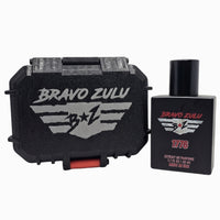 A product image of Bravo Zulu's 1776 Extrait de Parfum matte black cologne bottle standing next to its closed, rugged black tactical storage case on a plain white background. The heavy-duty case prominently features a silver-gray debossed tactical wings logo and a crimson red latch, while the bottle label showcases the matching silver wings emblem and prominent red 1776 text. This setup represents the high-performance presentation of the American-made, 30% oil concentration masculine Bay Rum fragrance line.