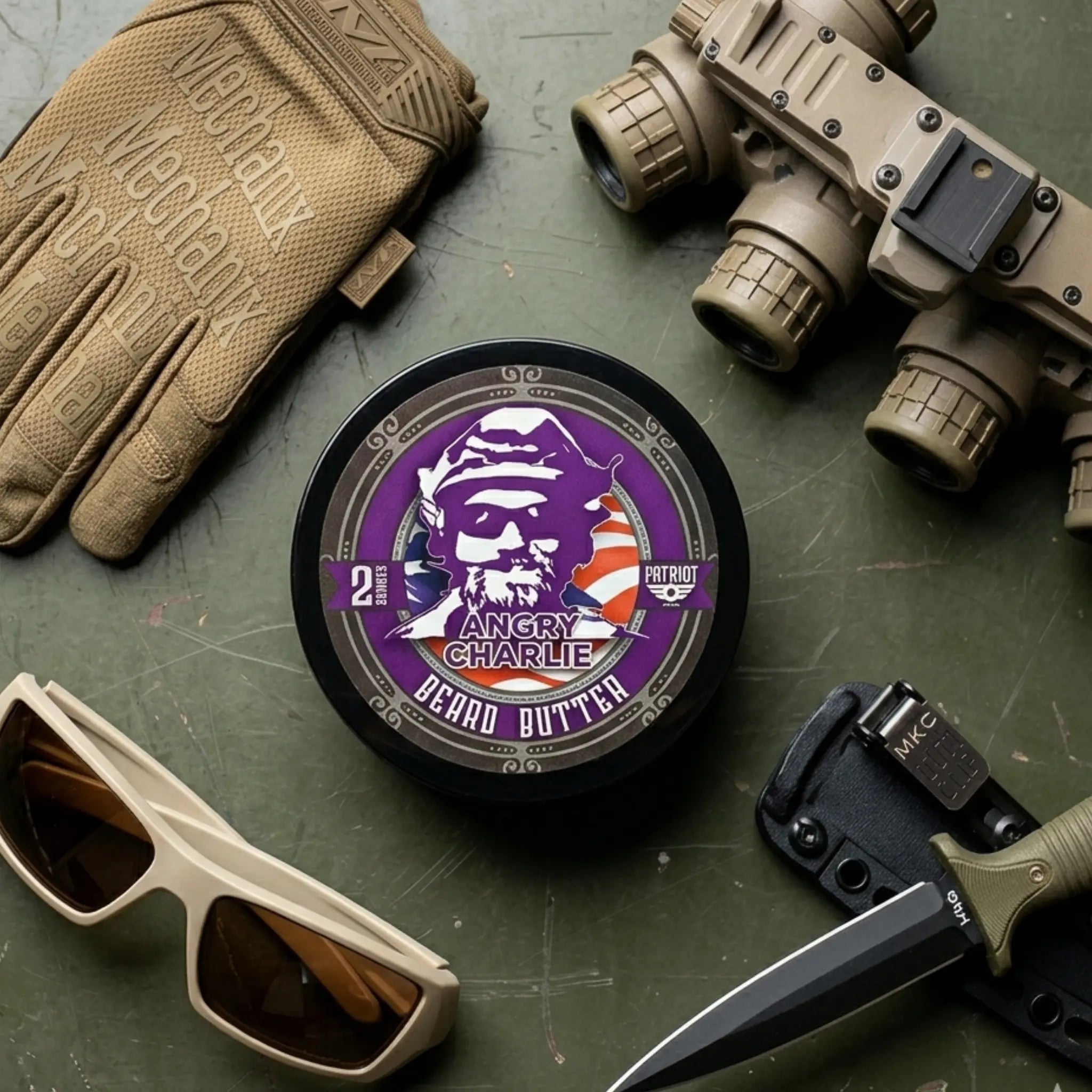 Flagship Soap Company Angry Charlie beard butter tin featuring the purple bearded skull logo, surrounded by professional tactical equipment and an MKC knife.