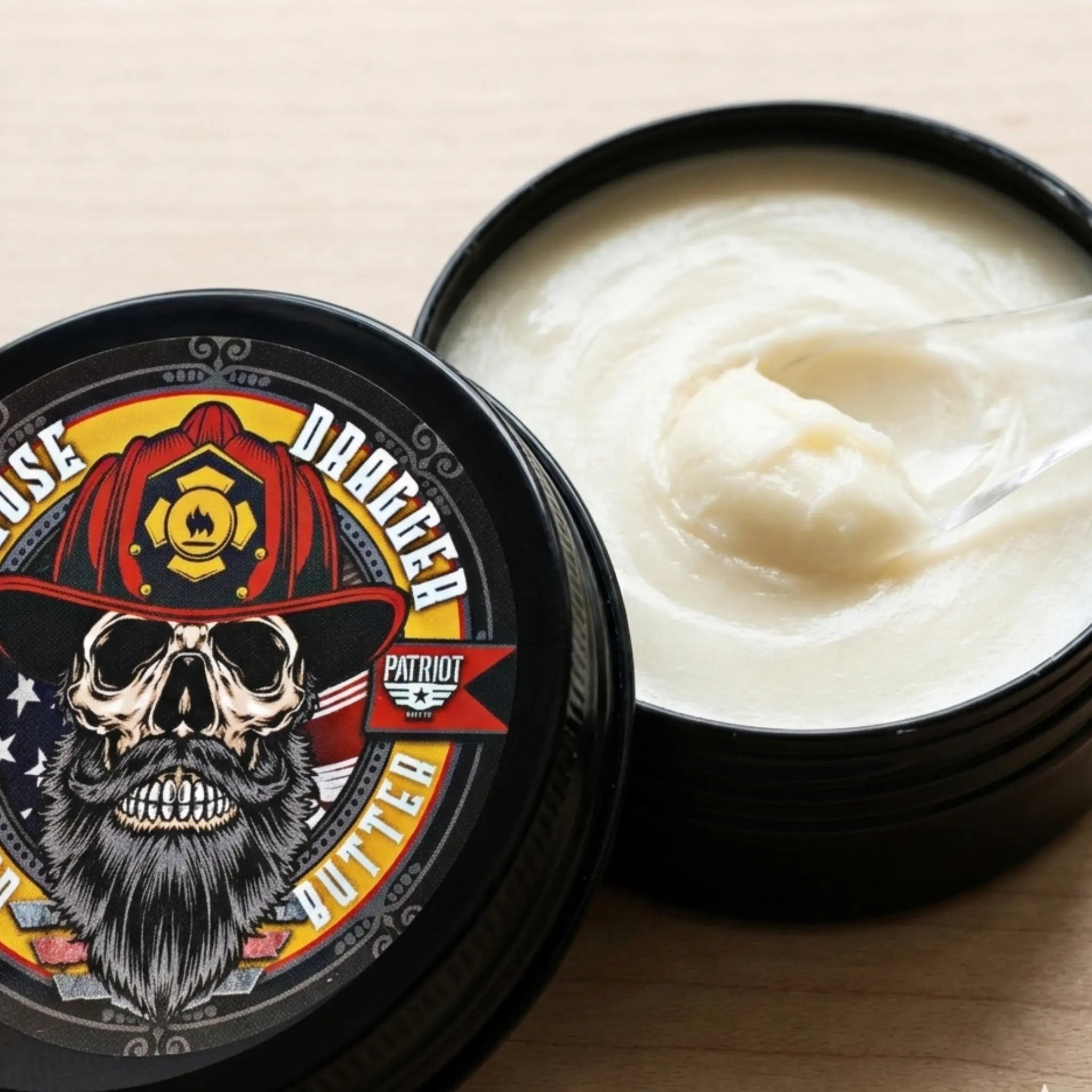 A close-up view of an open 2 oz tin of Hose Dragger beard butter, showing the smooth, whipped white texture of the premium grooming balm next to the firefighter-themed lid.