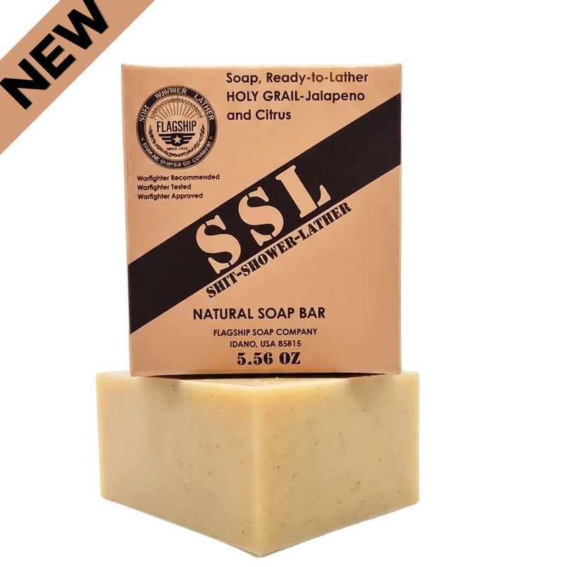 A studio shot featuring the Holy Grail Natural Soap by Flagship Soap Company on a clean white background. The packaging is a direct nod to military Meals Ready to Eat (MRE), labeled as "Soap, Ready-to-Lather" with a bold "SSL" (Shit-Shower-Lather) diagonal stripe. The tan box sits on top of a thick, natural, cream-colored soap bar and displays the "Warfighter Tested" seal. This rugged, MRE inspired bar is a great gift idea for any veteran or first responder looking for high-quality, Idaho-made natural groom