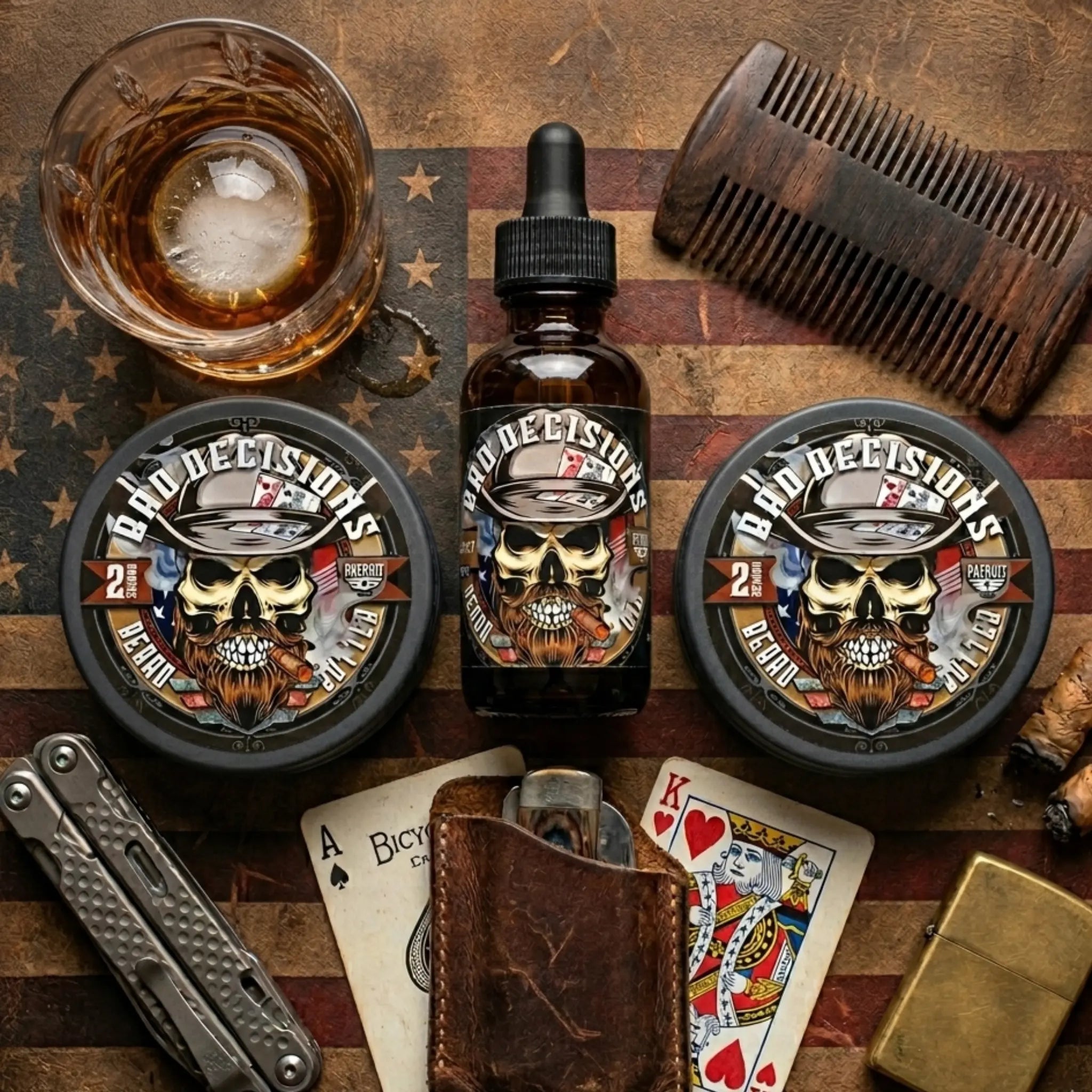An overhead flatlay of Bad Decisions Beard Oil and Butter on an American flag background, surrounded by a glass of bourbon, a pocket knife, and a comb. The products are scented like Buffalo Trace charred oak barrels and whiskey.