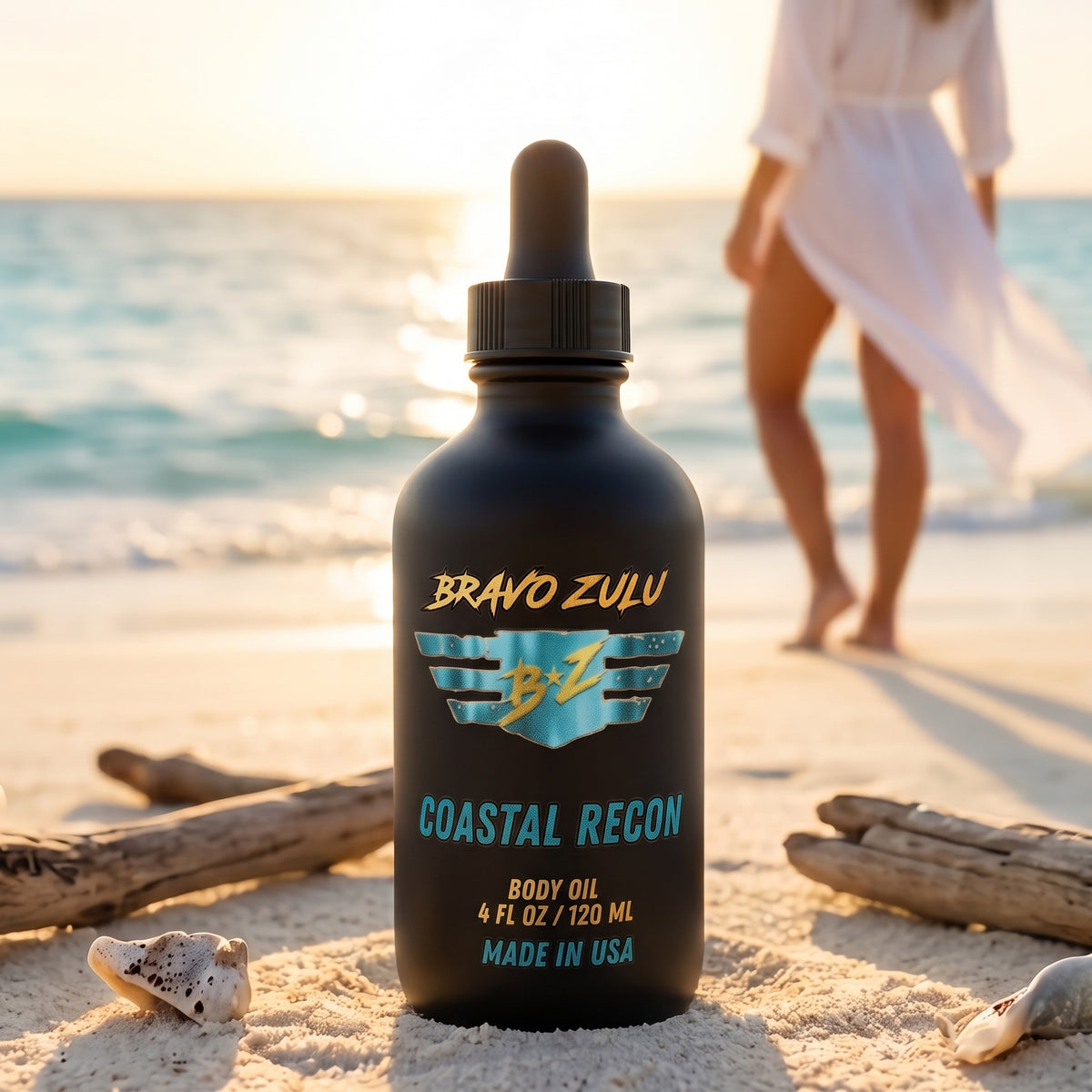 Bravo Zulu Coastal Recon Body Oil dropper bottle on a sunlit beach with driftwood and seashells, matte black glass with turquoise and gold Bravo Zulu B★Z logo