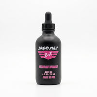 Bravo Zulu Merican Woman Body Oil dropper bottle on a sandy beach with an American flag and ocean waves in the background, pink Bravo Zulu B★Z logo