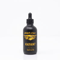 Bravo Zulu Radiant Body Oil dropper bottle studio product shot on white background, matte black glass with gold Bravo Zulu B★Z logo, 4 fl oz / 120 mL
