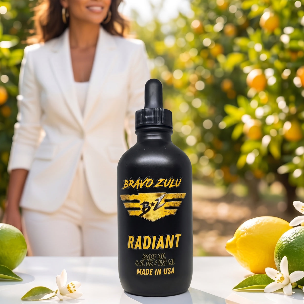 Bravo Zulu Radiant Body Oil and Extrait de Parfum bottles side by side on white background with citrus fruit and orange blossom flowers, gold and black Bravo Zulu B★Z logo