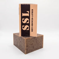 Side view of the "Brick Maker" soap box, showing the large, dark exfoliant bar and the vertically oriented "SSL" acronym, which tactically stands for "Shit-Shower-Lather." This hydrating bar soap is designed for physical jobs, featuring the Peanut Butter and Banana MRE scent profile. Paraben-free and sulfate-free.