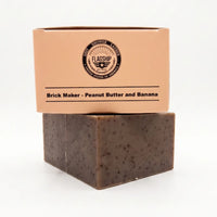 Frontal view of the Flagship Soap Company "Brick Maker" natural bar soap (5.56 OZ) in its beige box. The box displays the "Brick Maker: Peanut Butter and Banana" scent, the military-themed "Warfighter Approved" checklist, and "Flagship Idaho, USA B3815" crest. This massive, durable bar is hard-milled for a longer life and non-stripping cleanse.