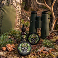Flagship Soap Company's "The Rut" beard products staged outdoors with hunting binoculars, an Eberlestock pack, and elk antlers. This heavy-duty balm and oil prevent itching and maintain healthy hair for the active outdoorsman. Scent Profile: Crisp Cedarwood and Pine.