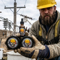 A heavily bearded electrical lineman in a yellow hard hat and work gloves kneels outdoors, holding a bundle of three Patriot Beard Co. 'Dirty Hands Clean Money' products. The collection features two tins of beard butter and a glass dropper bottle of beard oil, all smelling of rugged leather and oakmoss. The background shows utility poles and power lines under an overcast sky.