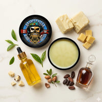 Flat lay of our top-selling Unsupervised Beard Butter with its signature masculine cologne scent, surrounded by natural shea butter, argan seeds, cocoa beans, and tea tree leaves.