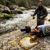 Premium top-selling Unsupervised beard oil pouring onto a river rock, highlighting the rich texture and signature masculine cologne fragrance.