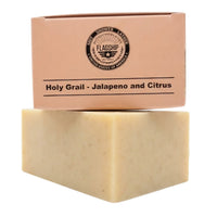 A bar of Holy Grail Natural Soap by Flagship Soap Company in Jalapeno and Citrus scent, featuring packaging inspired by military Meals Ready to Eat (MRE). The unboxed, tan natural soap bar sits below its tan cardboard box, which displays the Flagship Soap Company wings logo and the phrase "Shit Shower Lather." Designed to mimic the look of an MRE, this soap makes a unique and rugged gift for any veteran.